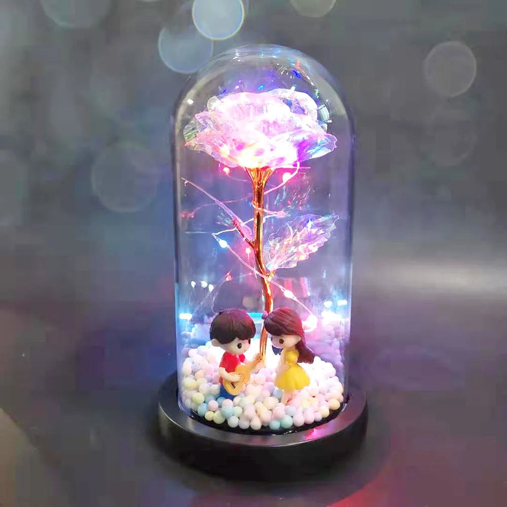 Gold artificial roses inside a clear glass dome ornament with LED lights and decorative accessories.