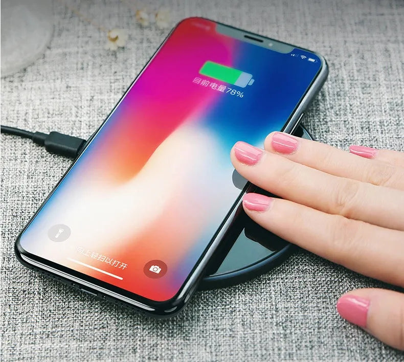 Black and white glass disc wireless charging pad for mobile phones on a wooden table.