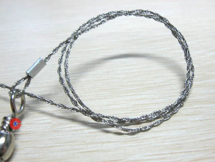 Coiled stainless steel survival wire saw with two black thumb rings, shown next to a ruler showing its 55cm length.