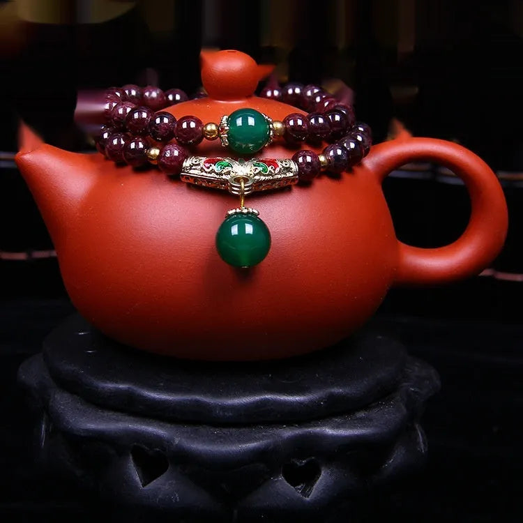Close-up of a women's bracelet with a 7mm round garnet in a double ring setting and a golden toad charm.