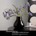Black ceramic round belly vase with coloured glaze finish and two white orchid flowers displayed on wooden surface