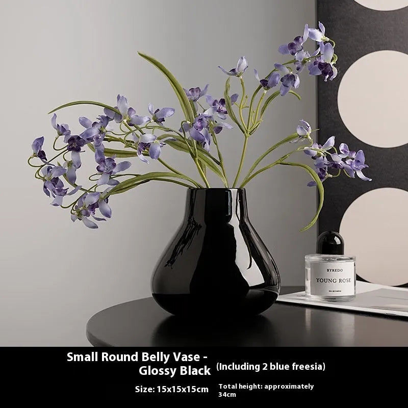 Black ceramic round belly vase with coloured glaze finish and two white orchid flowers displayed on wooden surface
