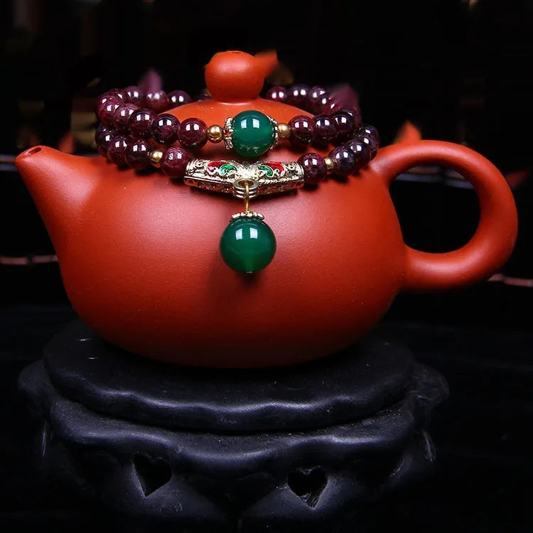 Close-up of a women's bracelet with a 7mm round garnet in a double ring setting and a golden toad charm.