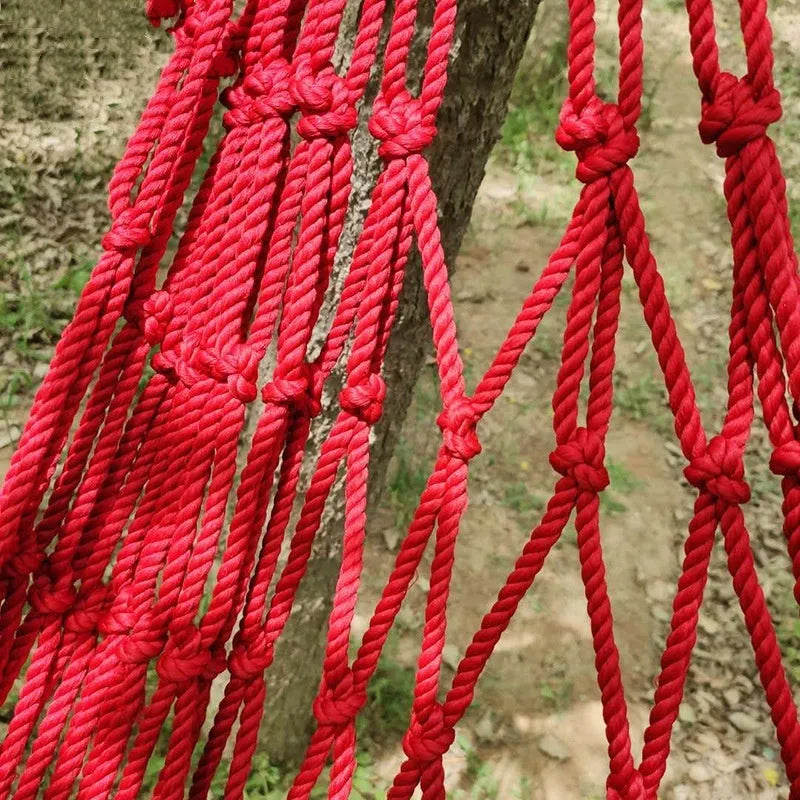 Green nylon rope mesh hammock hung between two trees with tying ropes.
