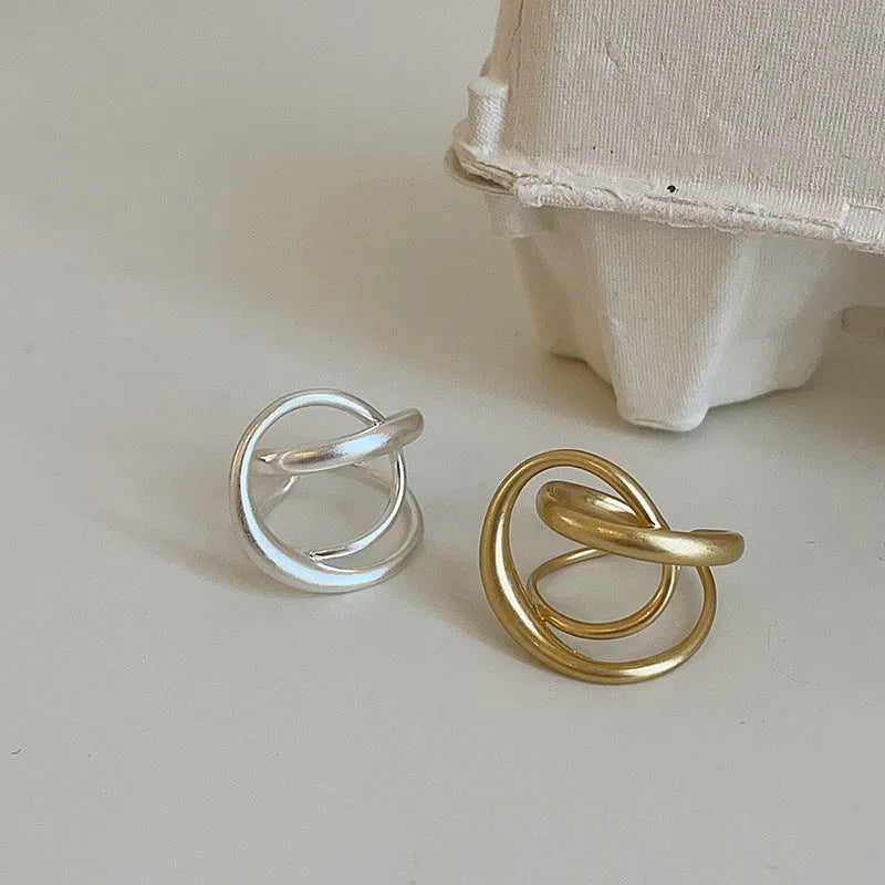 Adjustable geometric open ring with three-dimensional interlaced design and matte finish, shown in gold and silver colour options