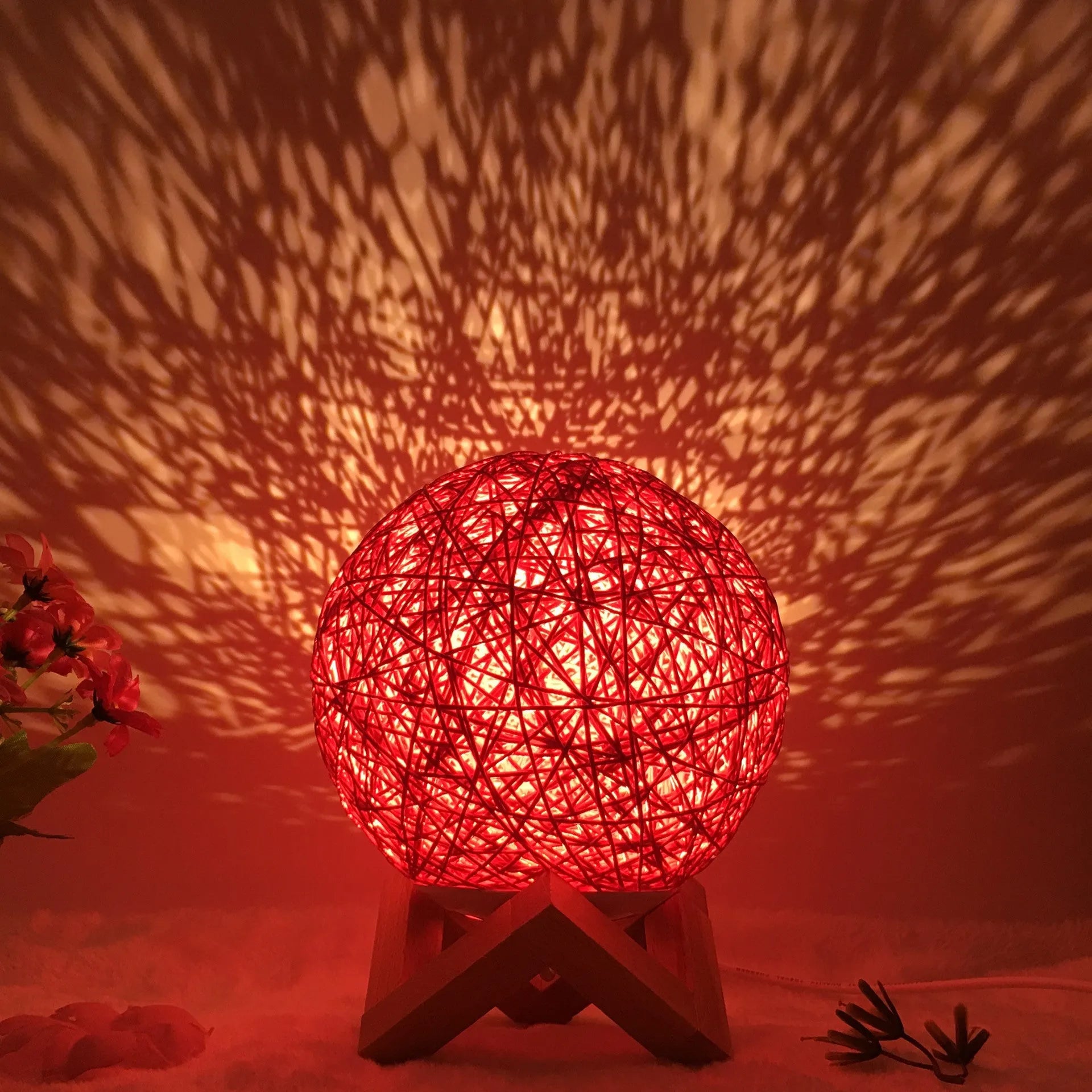 A hand-knitted rattan ball table lamp with a warm white LED glow, shown on a wooden surface.