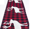 Red, white, and green Christmas table runner with elk and snowman print on a wooden dining table.