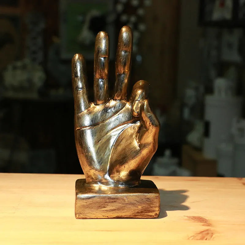 Bronze and silver resin hand gesture ornaments on a wooden desk, showing like, ok, and scissors hand signs.
