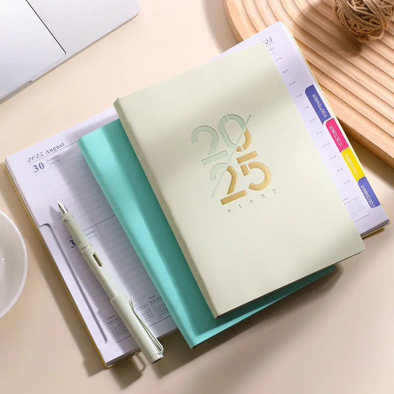 2025 A5 schedule book with faux leather cover in blue, showing open pages on a desk
