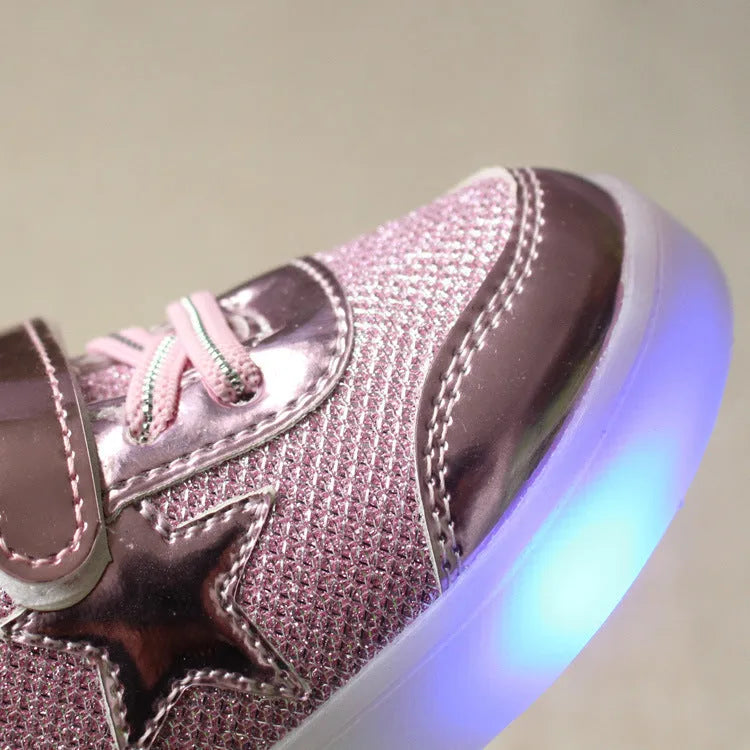 Set of golden, pink, and silvery LED light-up shoe buttons with glitter laces on a trainer.