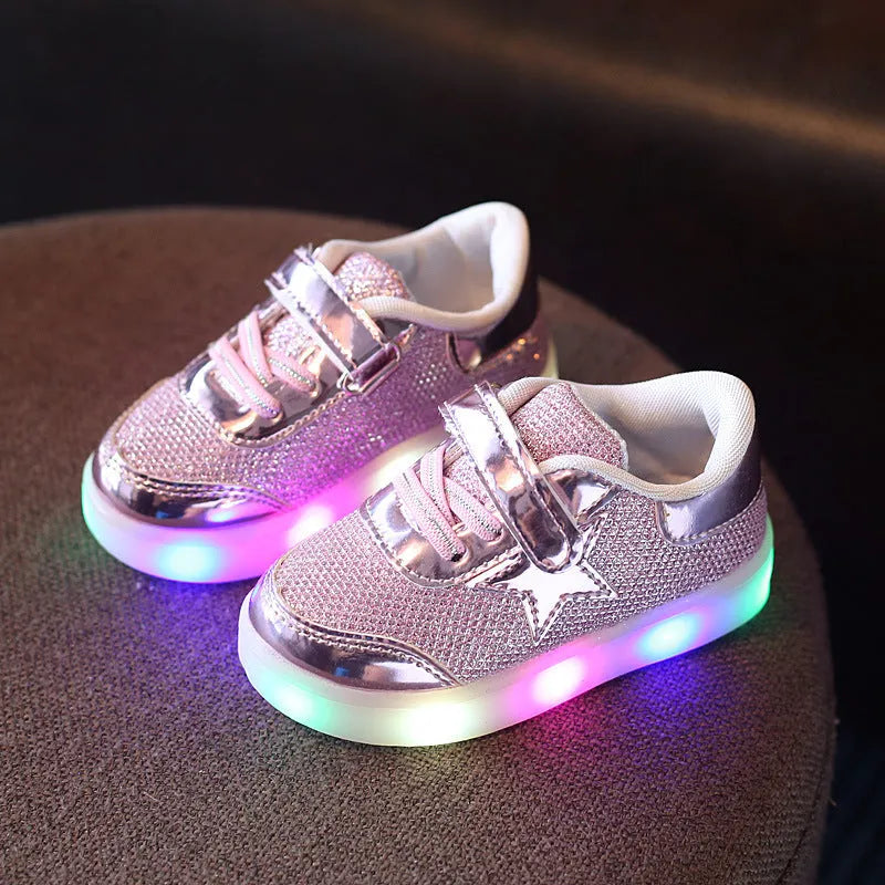 Set of golden, pink, and silvery LED light-up shoe buttons with glitter laces on a trainer.