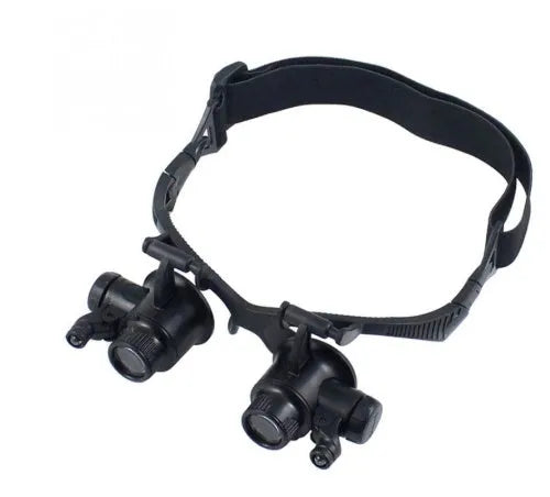 Black hands-free magnifier glasses with LED lights and four pairs of interchangeable magnification lenses on a workbench.