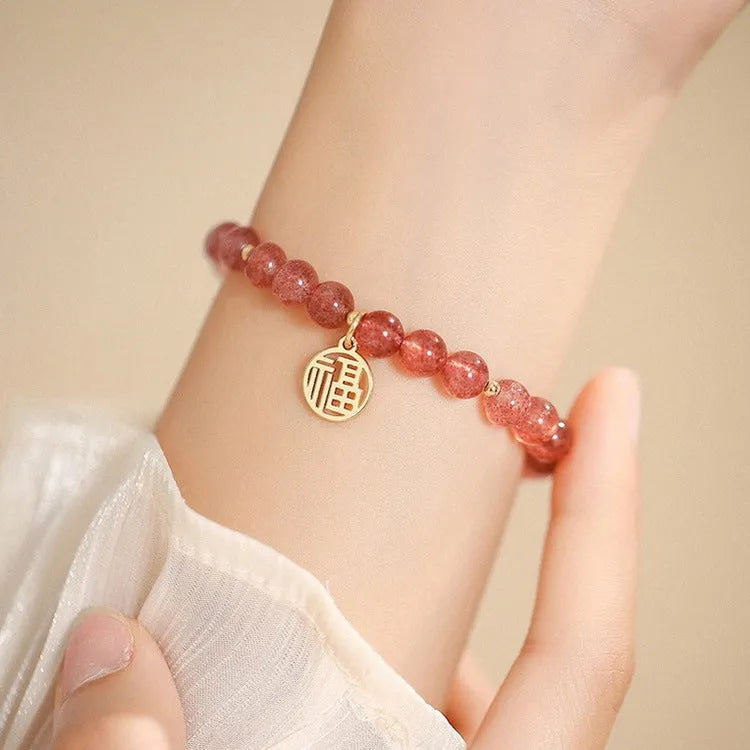 Handmade strawberry quartz style glass bead bracelet with a blessing card charm on a wrist.