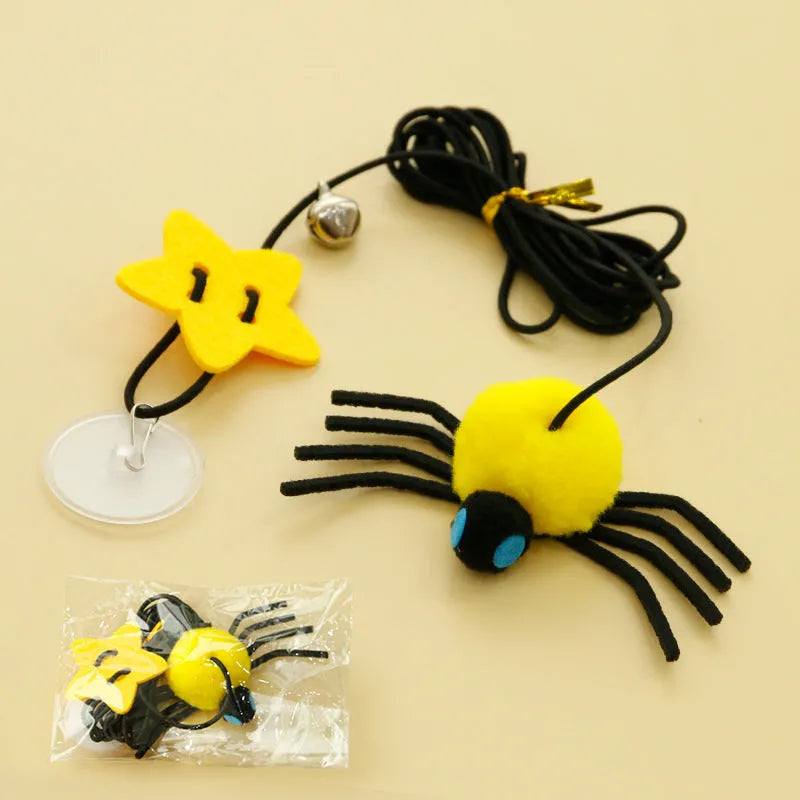 Red and yellow elastic rope cat toy hanging from a door, with feathers, a plastic spider, and a bell.