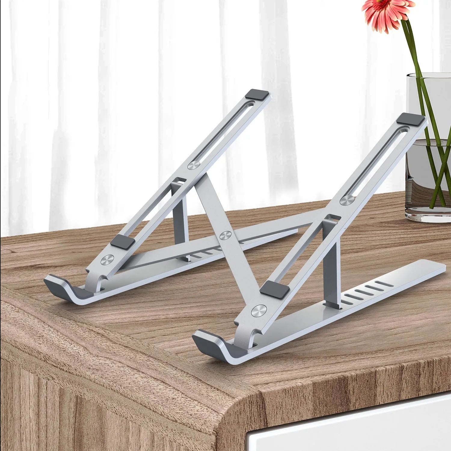 Silver aluminium laptop stand with six-height adjustment gears beside a black laptop on a desk