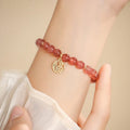 Handmade strawberry quartz style glass bead bracelet with a blessing card charm on a wrist.