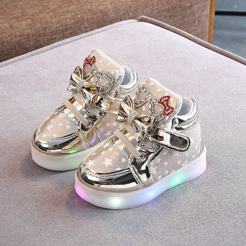 Set of golden, pink, and silvery LED light-up shoe buttons with glitter laces on a trainer.