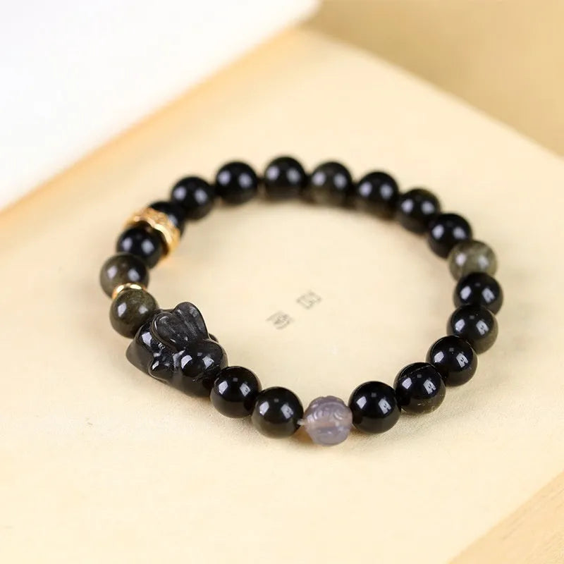 Handmade grey obsidian lying rabbit bracelet with brass and silver details on a wrist, shown in 8mm and 10mm size options.