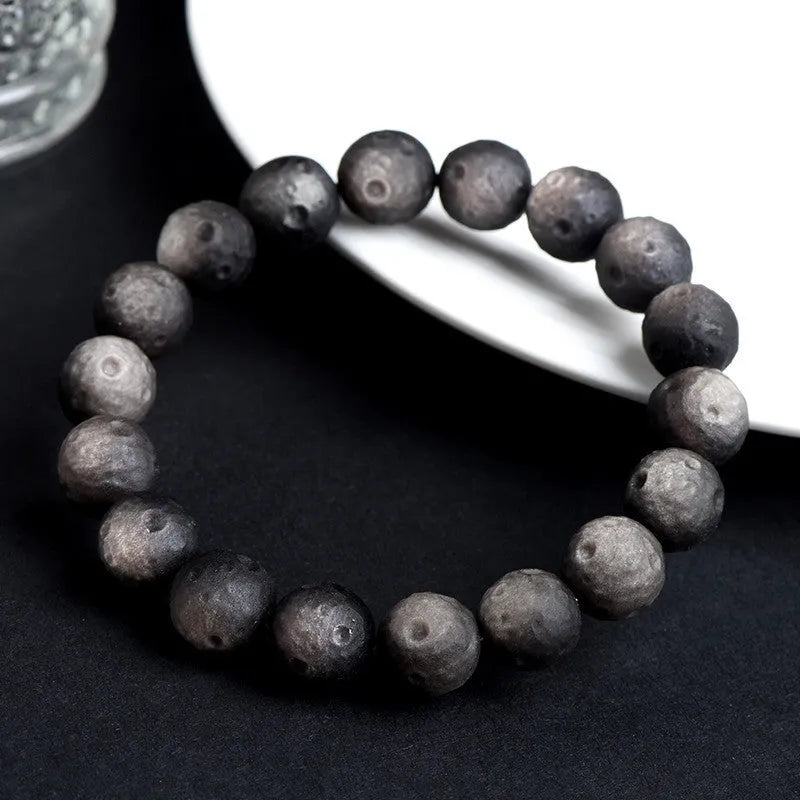 Natural obsidian crater ball bracelet with hand-ground texture, showing silver stone meteorite colour variation