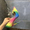 Rainbow coloured patent leather high-heel shoes with a thin stiletto heel and pointed toe on a white background.