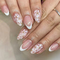 Short almond-shaped artificial nails with white French tips and glittering powder flower designs on translucent base