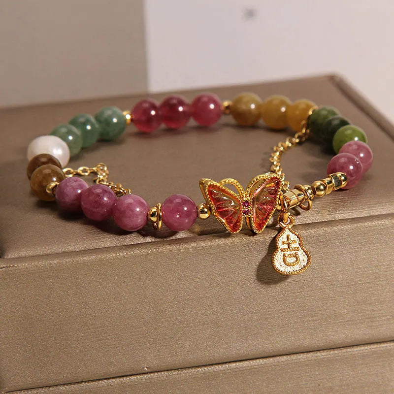 Close-up of a women's agate and tourmaline charm bracelet with butterfly and gourd shapes on a white background.
