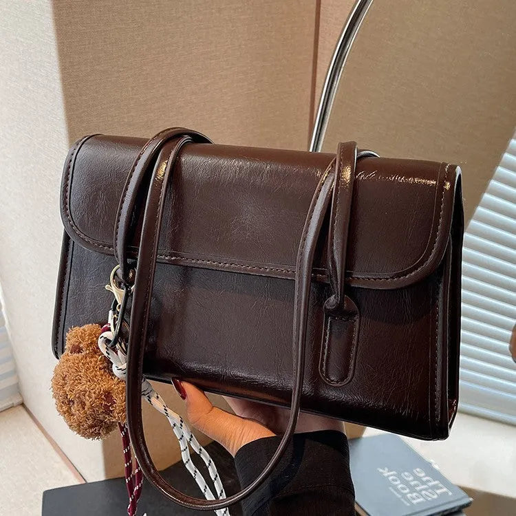 Brown women's structured shoulder bag with horizontal square shape, pendant accessory, and double joint shoulder straps