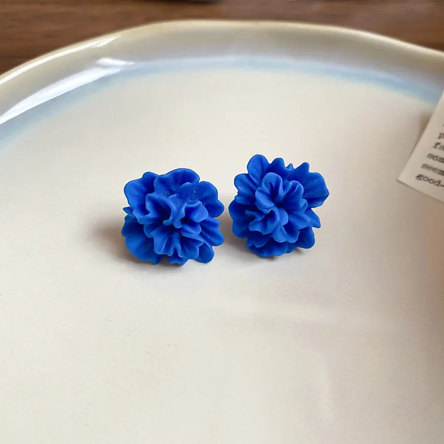 Women's geometric earrings with blue resin flower and silver needle on cloth background