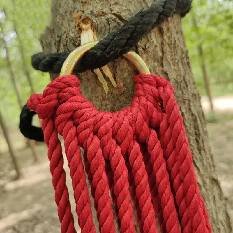 Green nylon rope mesh hammock hung between two trees with tying ropes.