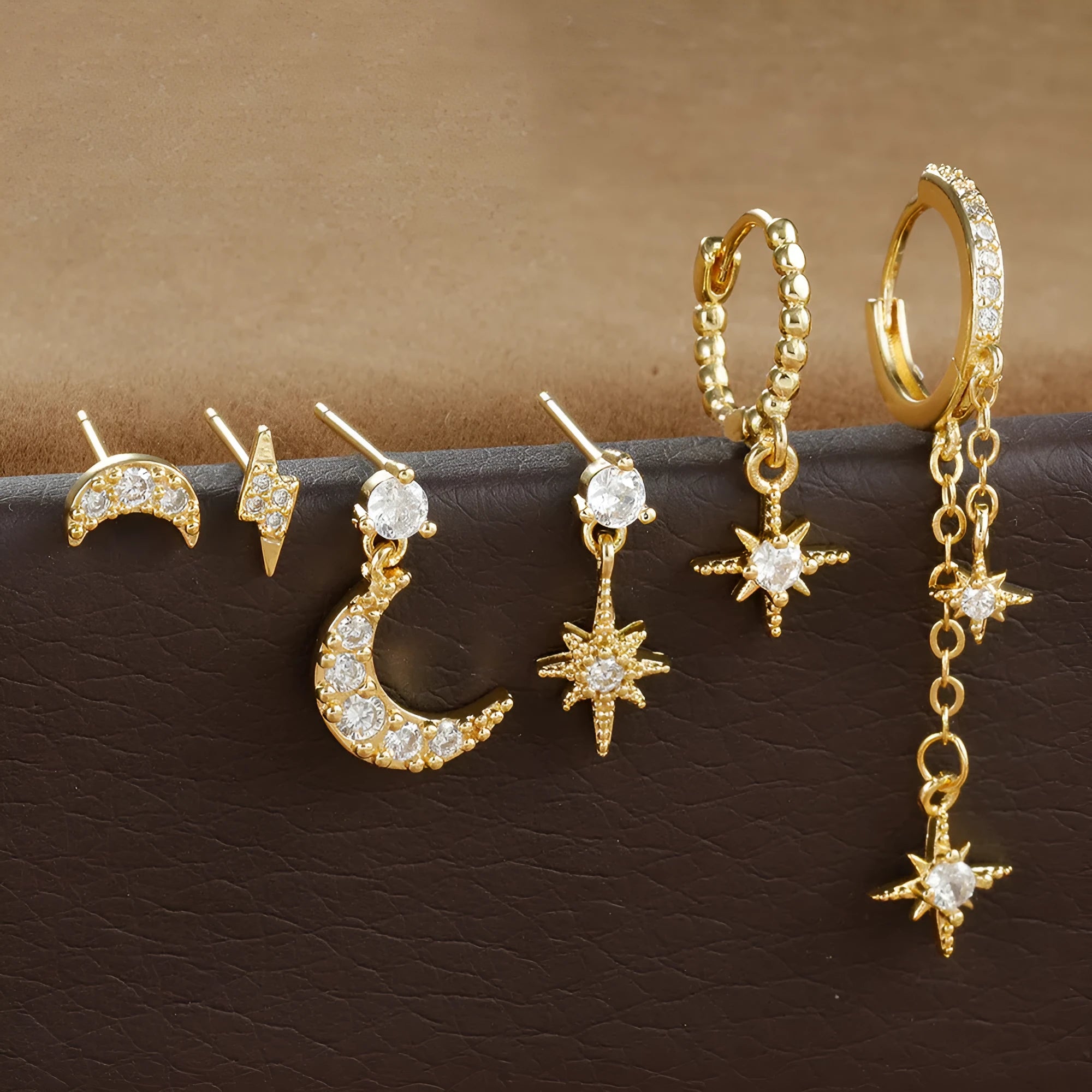 XINGX set of six gold chain tassel and zircon stud drop earrings laid out on a dark surface