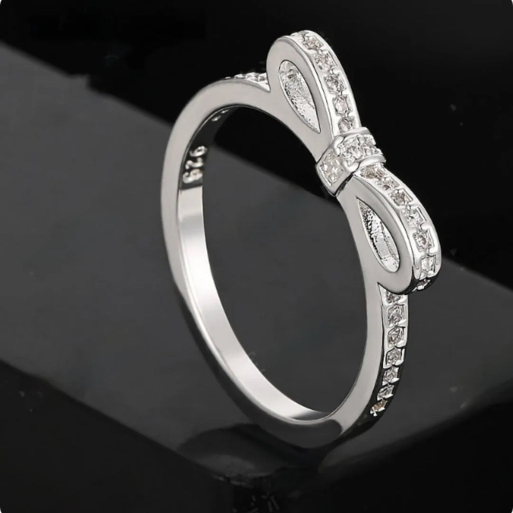 Silver bow-shaped ring with zircon crystal accents on finger, showing electroplated finish and detailed bow structure