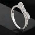Silver bow-shaped ring with zircon crystal accents on finger, showing electroplated finish and detailed bow structure