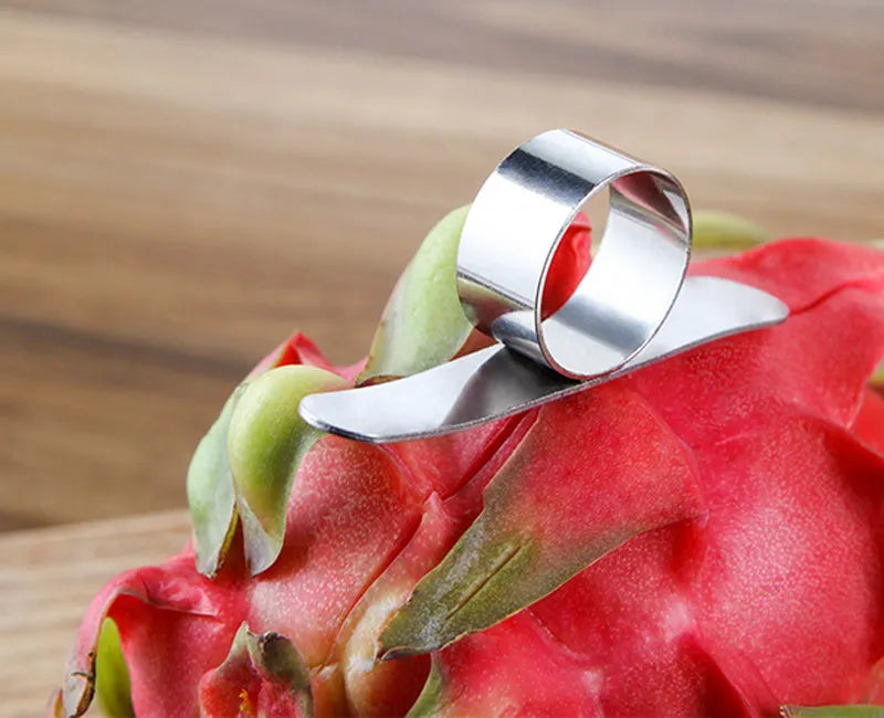A silver stainless steel finger-ring style citrus peeler for oranges and pomelo on a kitchen surface.