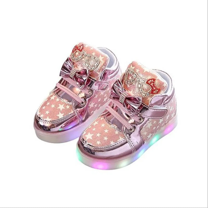 Set of golden, pink, and silvery LED light-up shoe buttons with glitter laces on a trainer.