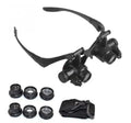 Black hands-free magnifier glasses with LED lights and four pairs of interchangeable magnification lenses on a workbench.
