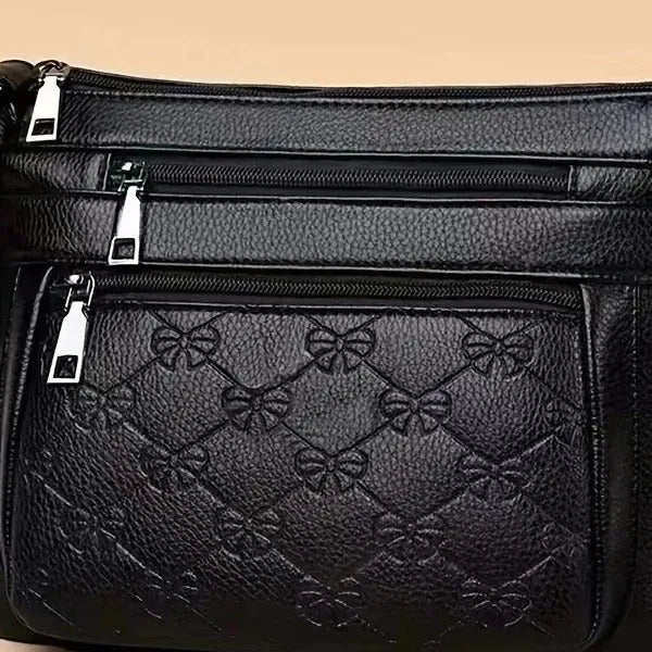 Women's black messenger bag with crossbody strap showing embossed detailing and exterior slit pocket