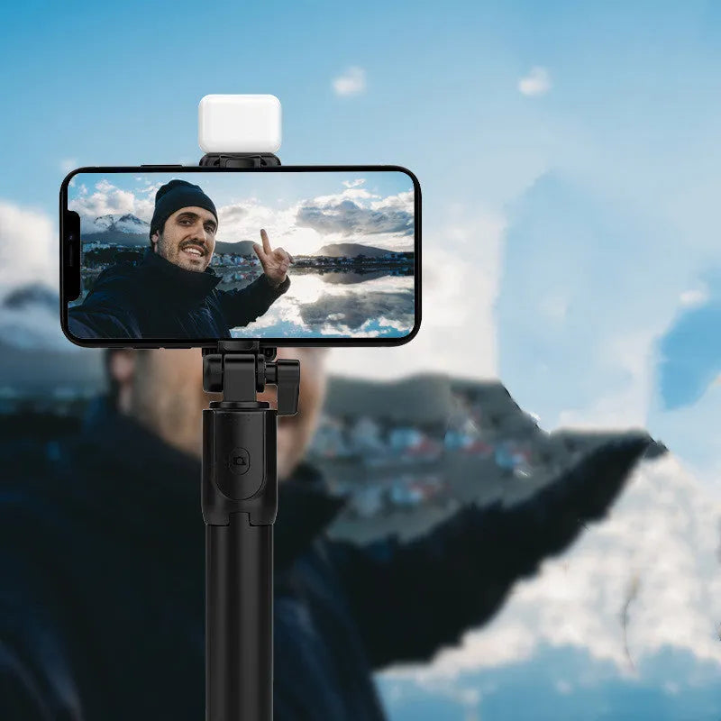 Black Bluetooth selfie stick with integrated tripod legs extended, showing 360-degree rotation mechanism and phone holder