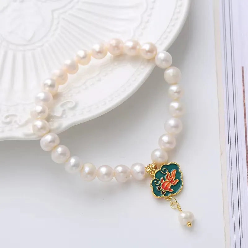 White freshwater pearl and gold electroplated lotus goldfish pendant on an antique style women's bracelet.