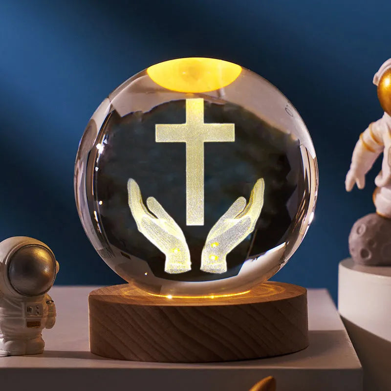 White crystal sphere on wooden base with warm glow, showing religious symbols including cross and prayer hands