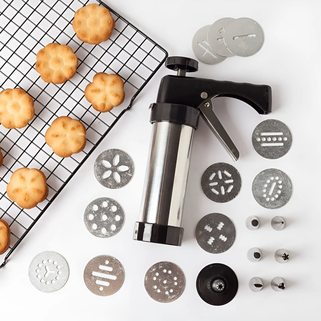 Stainless steel biscuit press gun with assorted cookie moulds and piping nozzles on a baking tray.