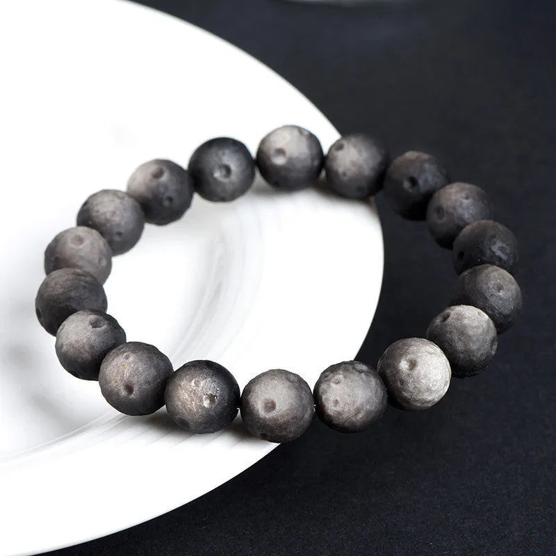 Natural obsidian crater ball bracelet with hand-ground texture, showing silver stone meteorite colour variation