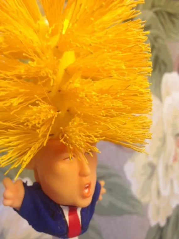 Yellow plastic Trump novelty toilet brush with a hanging slot on the handle.