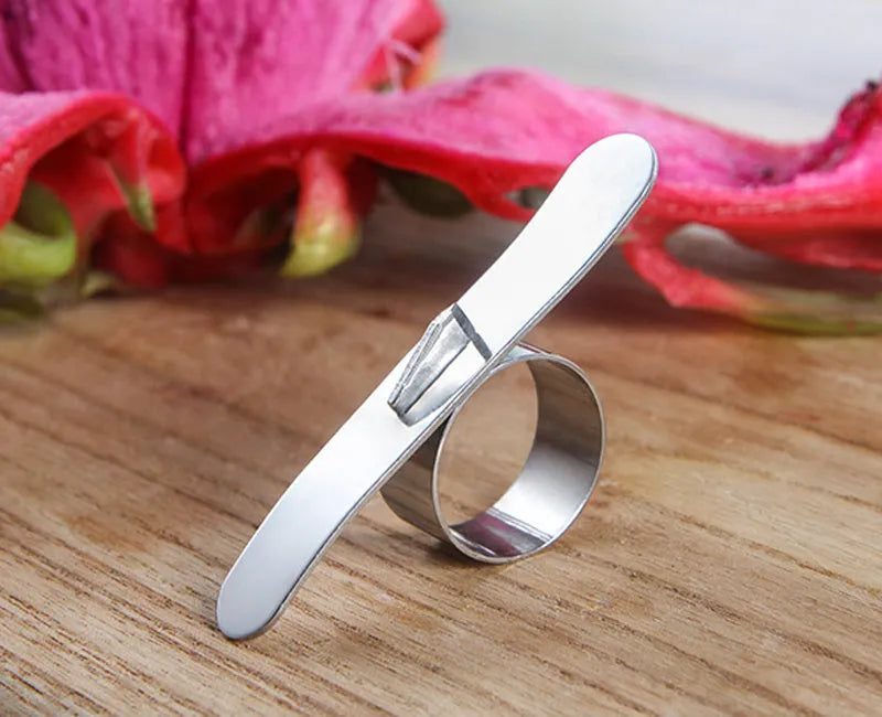 A silver stainless steel finger-ring style citrus peeler for oranges and pomelo on a kitchen surface.