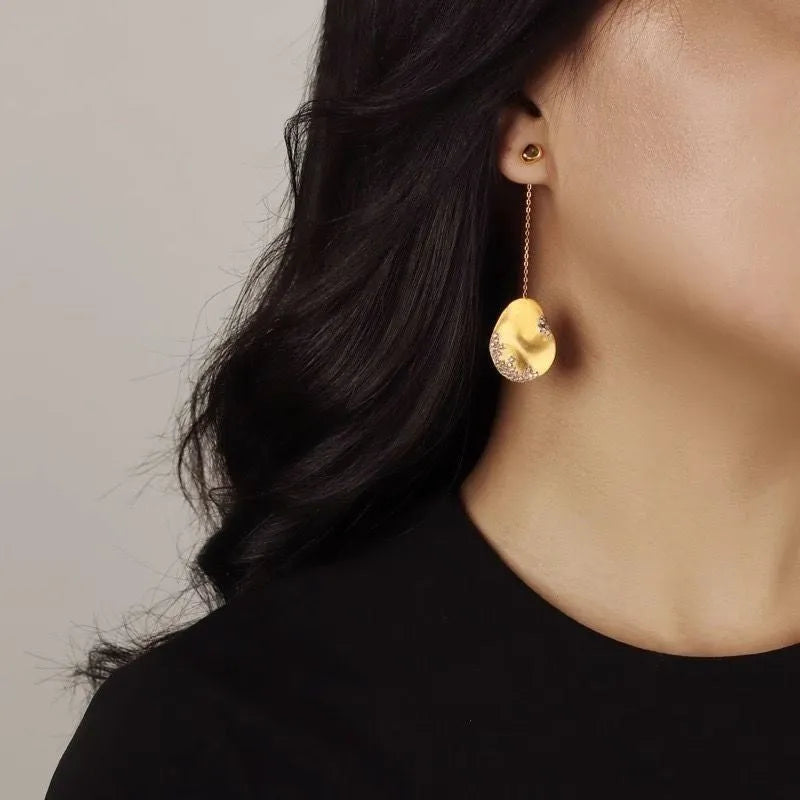 Asymmetric gold and silver floral drop earrings with clear zircon stone detailing on a white background.