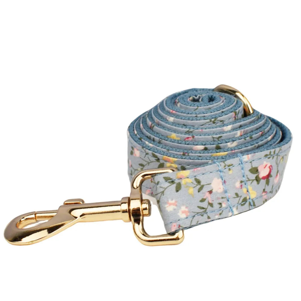 Blue floral pattern dog collar set with matching leash, vest, bow, and poop bag holder on wooden background