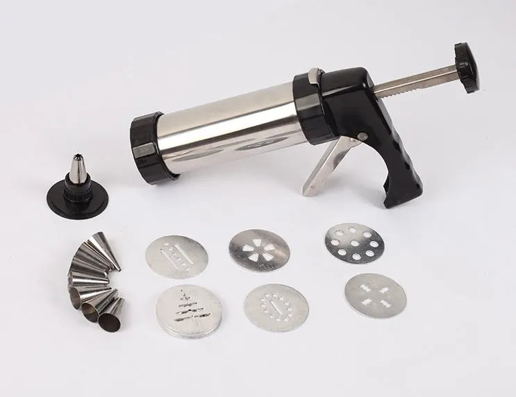 Stainless steel biscuit press gun with assorted cookie moulds and piping nozzles on a baking tray.