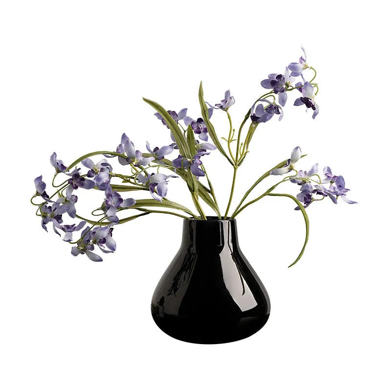 Black ceramic round belly vase with coloured glaze finish and two white orchid flowers displayed on wooden surface