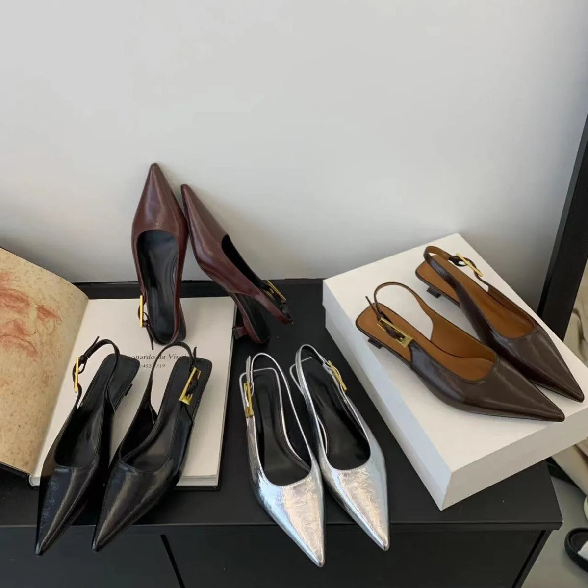 Women's black leather pointed toe shoes with a thin ankle strap and a low block heel.