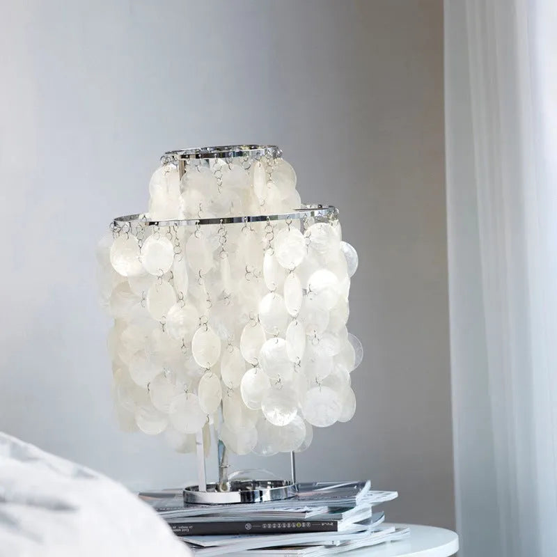 Modern shell-shaped bedside table lamp in a chrome finish on a wooden surface.