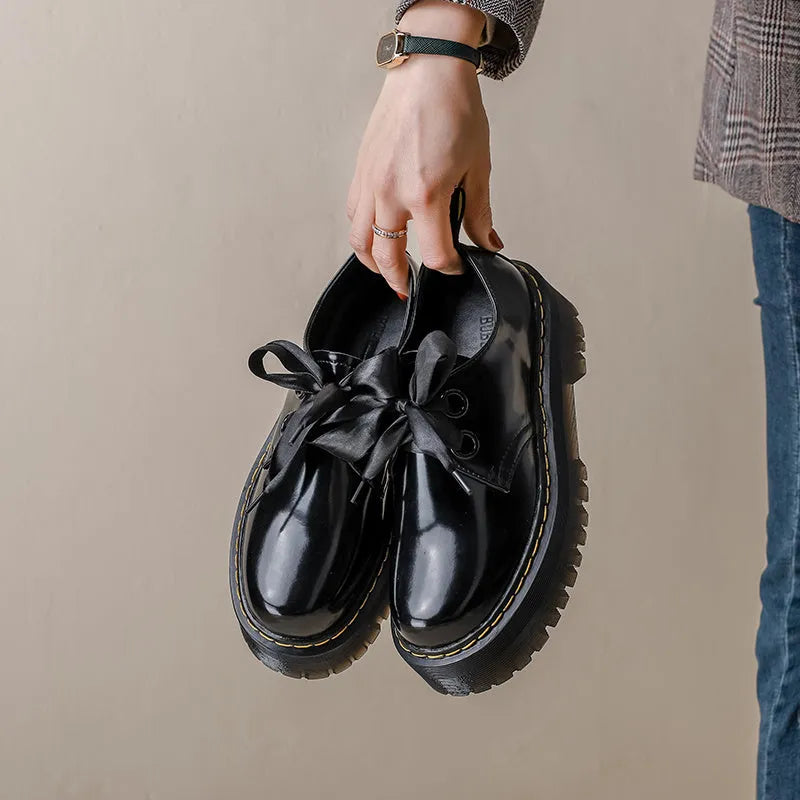 Women's black leather shoes with cross-strap design and thick TPR soles, showing ribbon detailing and lacing closure